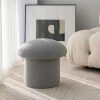 Puf tapizado en forma de seta, en color gris claro, colocado junto a una cama en un dormitorio de estilo minimalista.